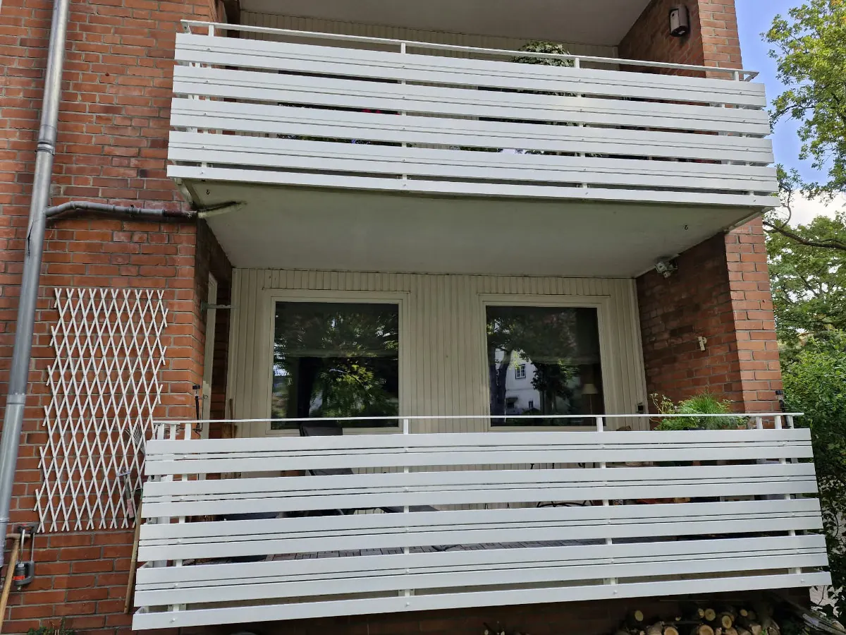 Seitenansicht von zwei Balkonen mit weiß pulverbeschichtetem Stahl-Balkongeländer mit waagerechter Lattung an einem Backsteinhaus